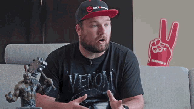 a man wearing a venom shirt sits on a couch next to a peace sign