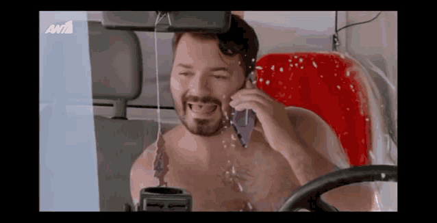 a shirtless man is talking on a cell phone in a car with the letters anta on the bottom right