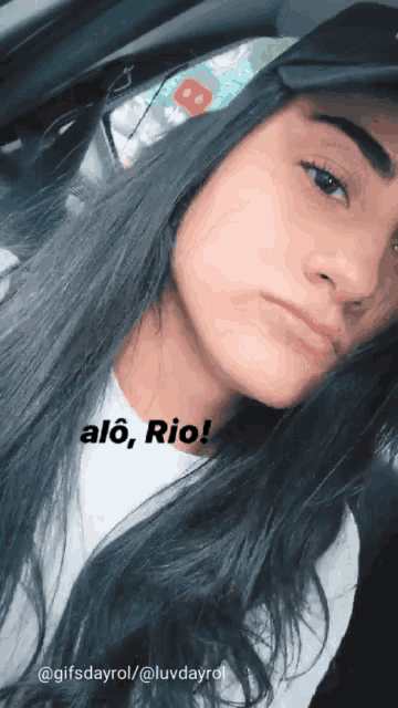 a girl with long dark hair is wearing a white shirt and a black hat and says alo rio