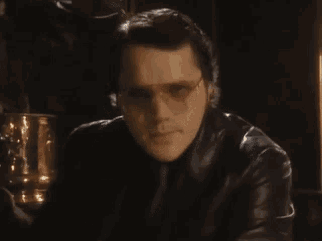 a man in a leather jacket says greetings traveler in a dark room