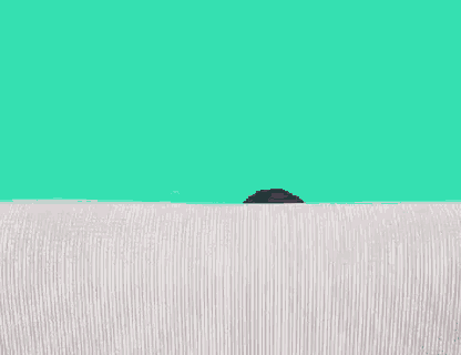 a woman is peeking over a couch against a green screen .