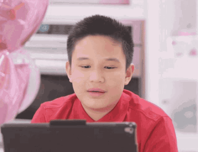 a boy in a red shirt looks at a tablet