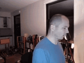 a man in a blue shirt stands in front of a bookcase