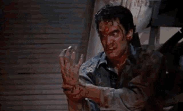 a man with blood on his face and hands is sitting in a chair .