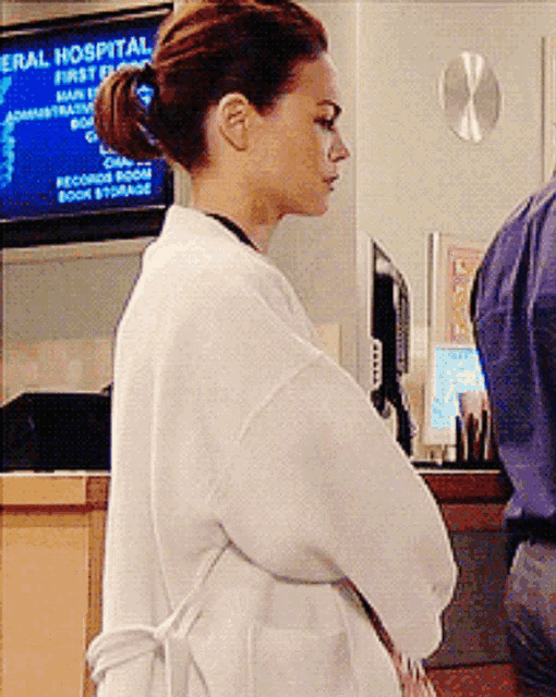 a woman in a white coat stands in front of a sign for the general hospital