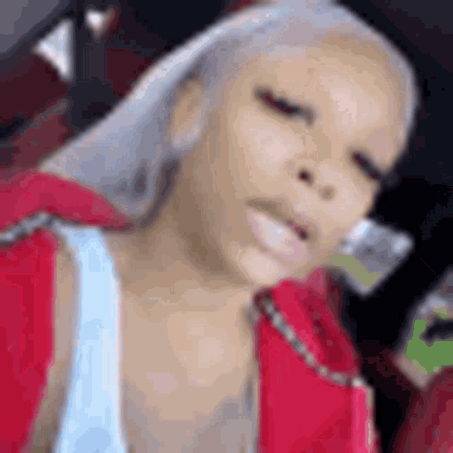 a woman with white hair is sitting in a car wearing a red jacket and a blue tank top .