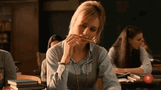a woman with a pencil in her mouth is sitting in a classroom