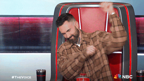 a man in a plaid shirt is sitting in a chair with a nbc logo on the bottom
