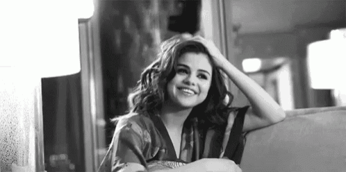 a black and white photo of a woman sitting on a couch with her hand in her hair .