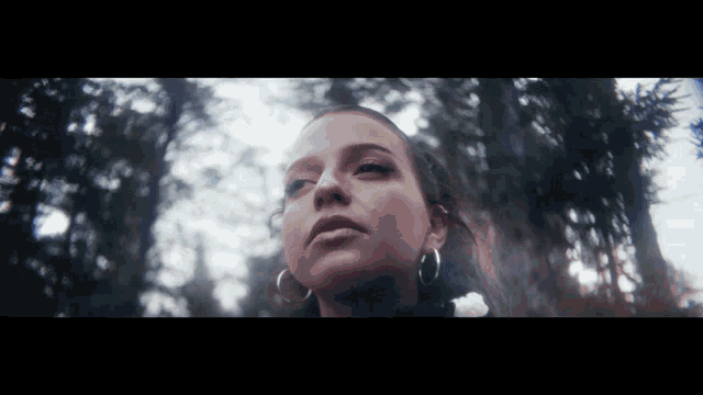 a woman wearing hoop earrings is standing in the woods
