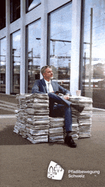 a man in a suit sits on a stack of newspapers in front of a building
