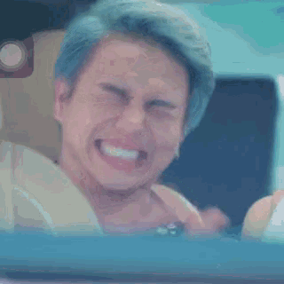 a man with blue hair is laughing while sitting in a car with his eyes closed .