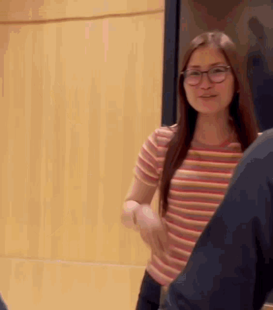 a woman wearing glasses and a striped shirt is standing in front of a wooden wall