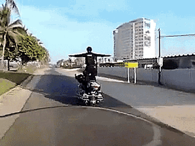 a man is riding a motorcycle down a city street with his arms outstretched
