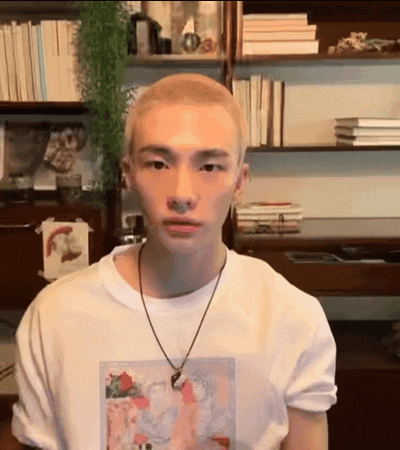 a young man with a shaved head wearing a white t-shirt and a necklace .