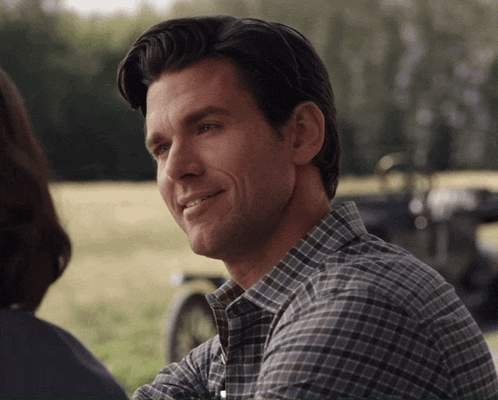 a man in a plaid shirt is smiling in front of a field