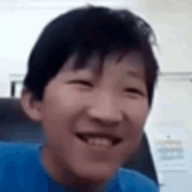 a young boy in a blue shirt is smiling while sitting in a chair .