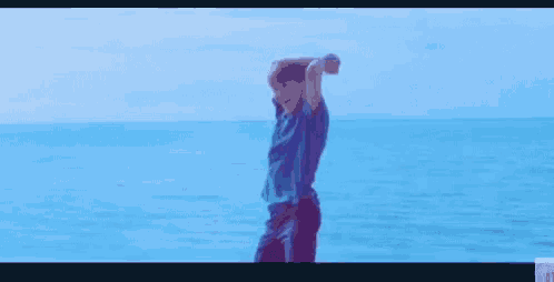 a man in a blue shirt is standing on the beach with his arms in the air .