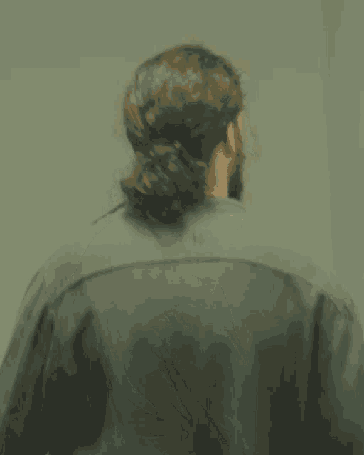 a man with long hair and a ponytail is wearing a grey shirt with the letter s on the back