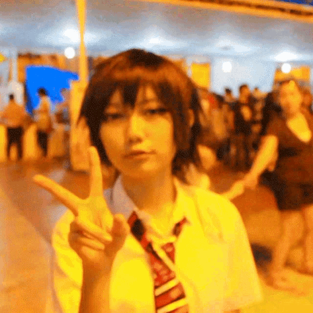 a woman in a yellow shirt and tie is giving a peace sign