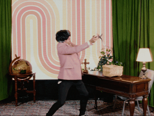 a woman in a pink jacket is dancing in front of a large screen with the letter u on it