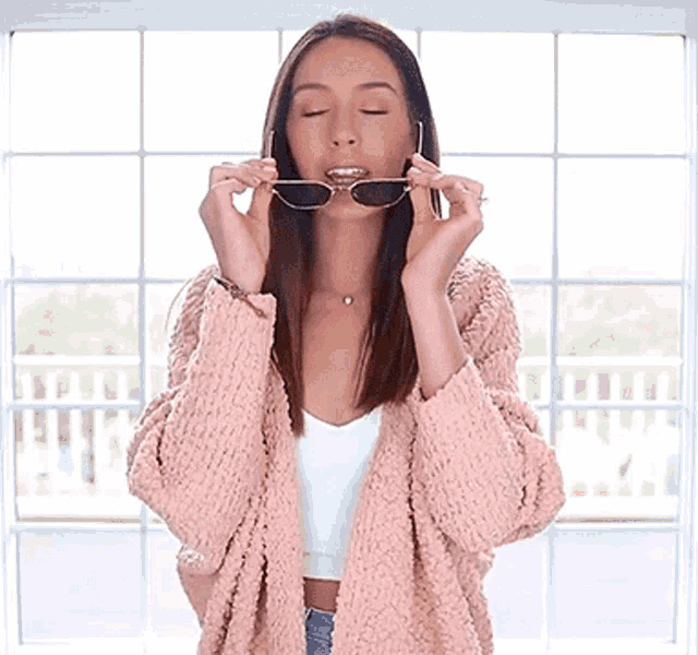 a woman in a pink sweater is holding her sunglasses over her face
