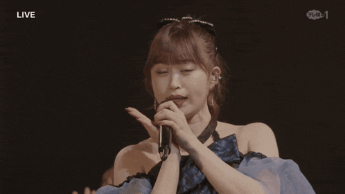 a woman is holding a microphone in front of her face and the word live is on the bottom right