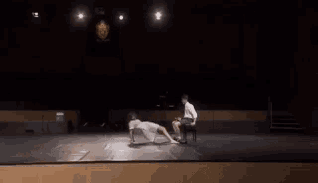 a man is sitting on a chair on a stage while a woman crawls on the floor .