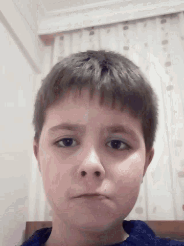 a close up of a young boy 's face with a blue shirt on