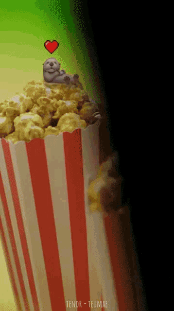 a striped container of popcorn with a sloth laying on top