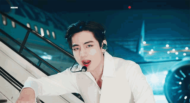 a man wearing a white shirt and a microphone is sitting on a staircase with an airplane in the background