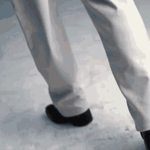 a person wearing white pants and black shoes is walking on a snowy surface .