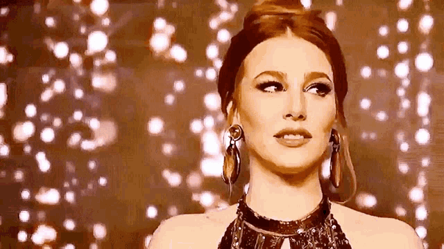 a woman wearing a necklace and earrings is standing in front of a wall of lights .