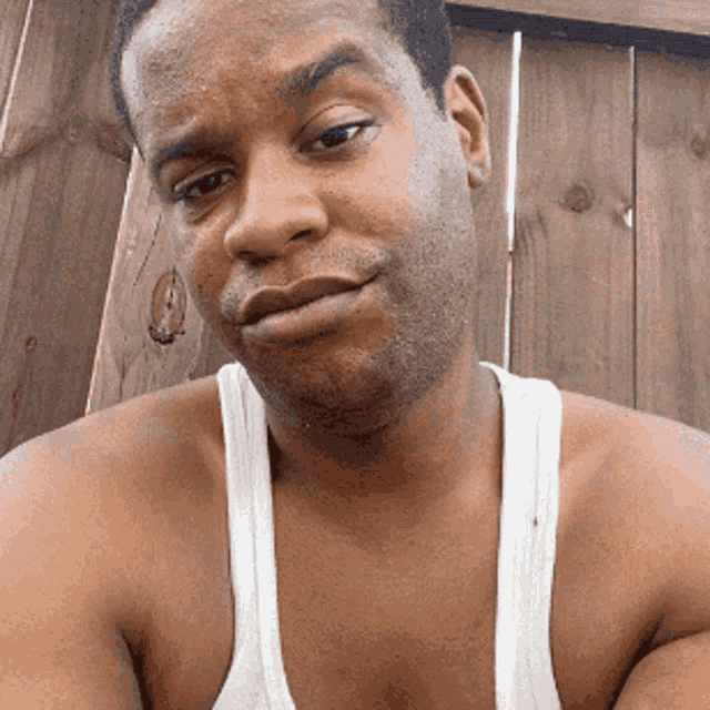 a shirtless man in a white tank top is looking at the camera