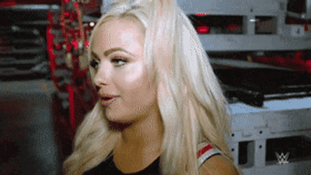 a woman with blonde hair is standing in front of a sign that says ' wwe ' on it