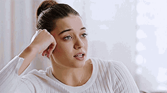 a woman wearing a white sweater is sitting on a couch .