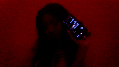 a woman is holding a cell phone in her hand in front of a red wall