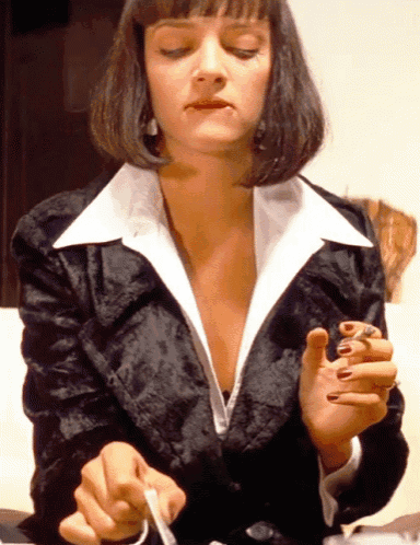 a woman in a black jacket and white collared shirt is smoking a cigarette with her eyes closed