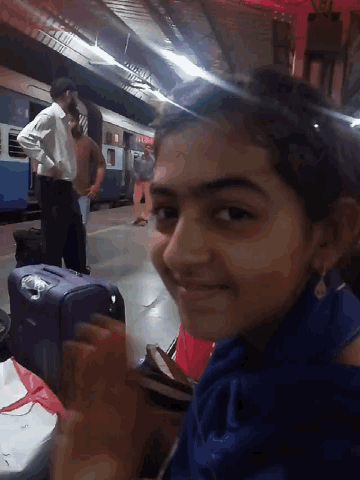 a girl smiles at the camera while a man stands behind her with a purple suitcase