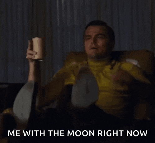 a man in a yellow shirt is sitting on a couch holding a cup and pointing at the moon .