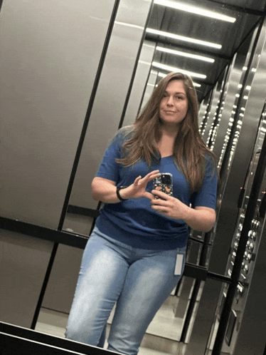 a woman in a blue shirt is taking a picture of herself in an elevator