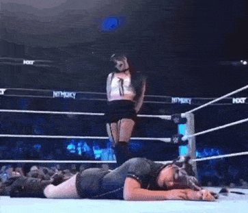 a woman in a white dress is standing in a wrestling ring with ropes .