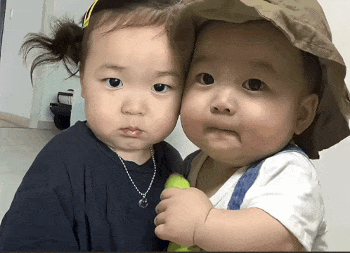 two babies are posing for a picture and one has a necklace on