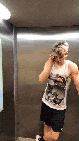 a man wearing a shirt that says obey is talking on a cell phone in an elevator