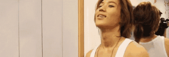 a man in a white tank top is looking at himself in the mirror .