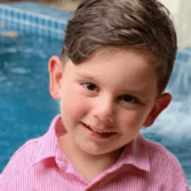 a young boy in a pink striped shirt is smiling in front of a swimming pool .