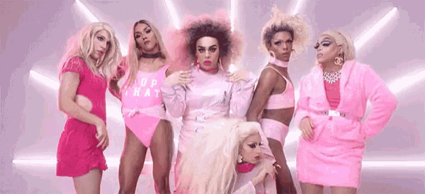 a group of drag queens are standing next to each other in pink clothes .