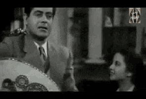 a man in a suit and tie is holding a fan while a woman looks on .