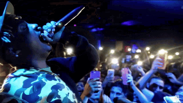 a man singing into a microphone in front of a crowd of people taking pictures