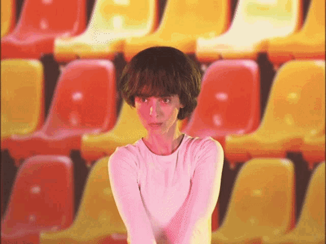 a woman in a white shirt is standing in front of a row of yellow and red chairs .